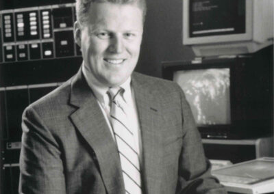 Historic photo of a meteorologist seated at a desk with weather maps and monitors in a WPTF weather center.