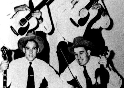 Black-and-white photo of a four-man bluegrass group wearing hats and holding instruments while gathered around a WPTF studio microphone.